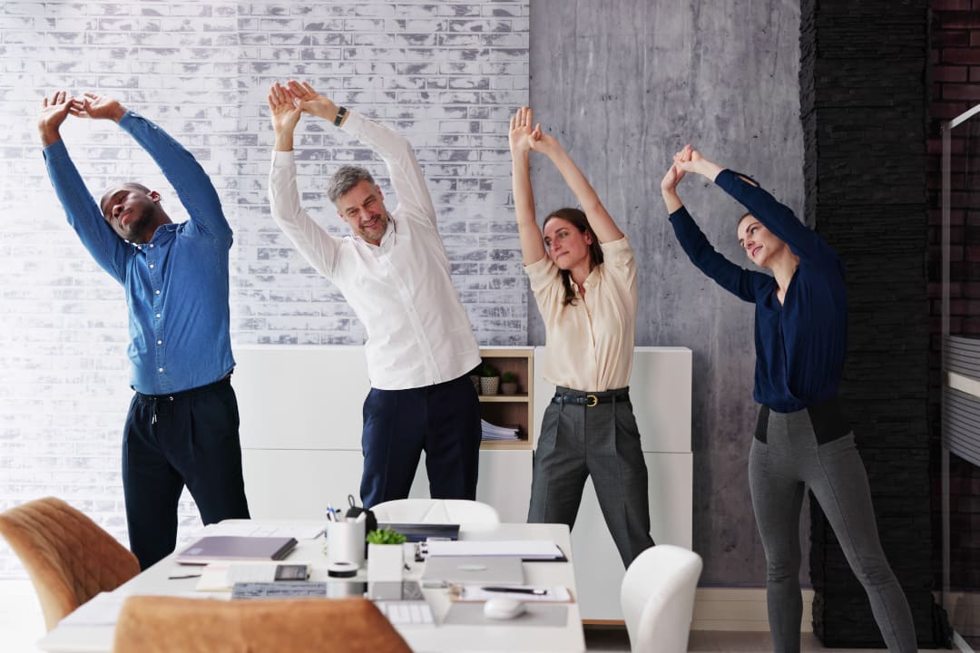 Büroteam macht gemeinsam Dehnübungen im Büro – Bewegung am Arbeitsplatz dank Corporate Health Programm